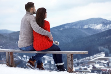 Photo of Couple sitting on bench and enjoying mountain landscape, space for text. Winter vacation