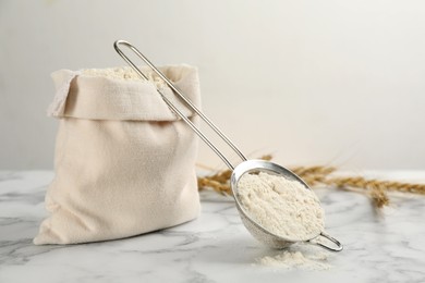 Photo of Sack and sieve with flour on white marble table