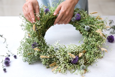 Photo of Woman making beautiful wreath of wildflowers at white table, closeup