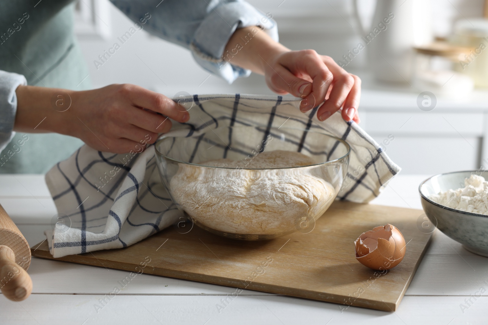 Photo of Woman covering dough with napkin at white wooden table in kitchen, closeup