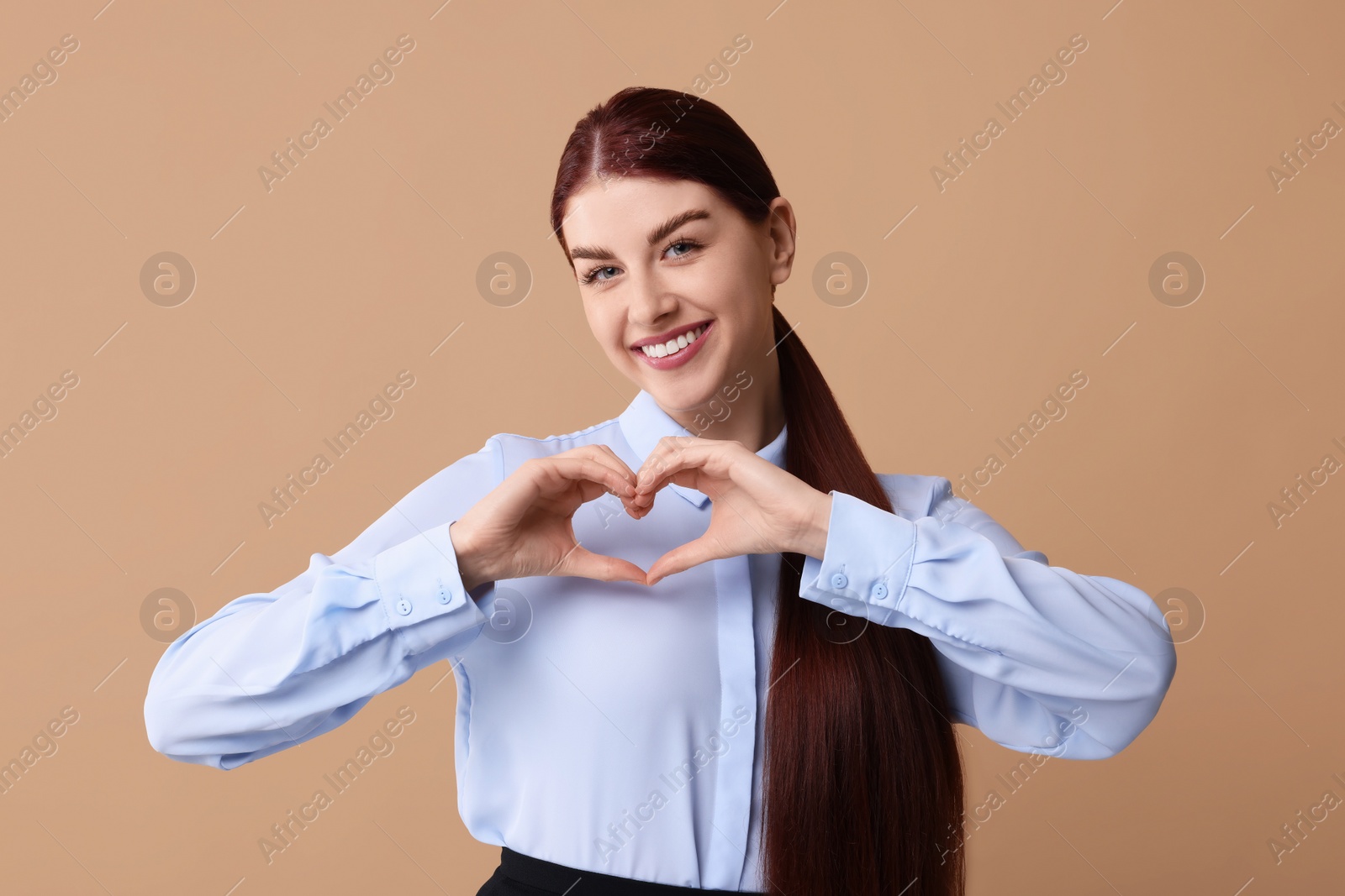 Photo of Happy young woman showing heart gesture with hands on beige background