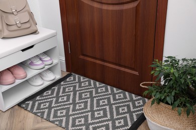 Photo of Stylish door mat, houseplant and storage with shoes in hall