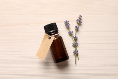 Bottle of essential oil and lavender flowers on white wooden table, flat lay