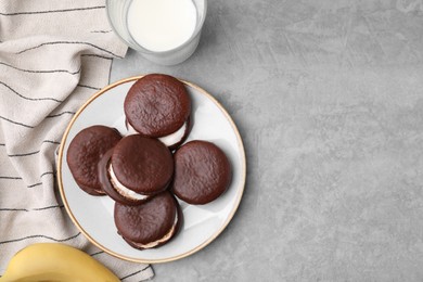 Photo of Tasty sweet choco pies, glass of milk and banana on light gray table, flat lay. Space for text