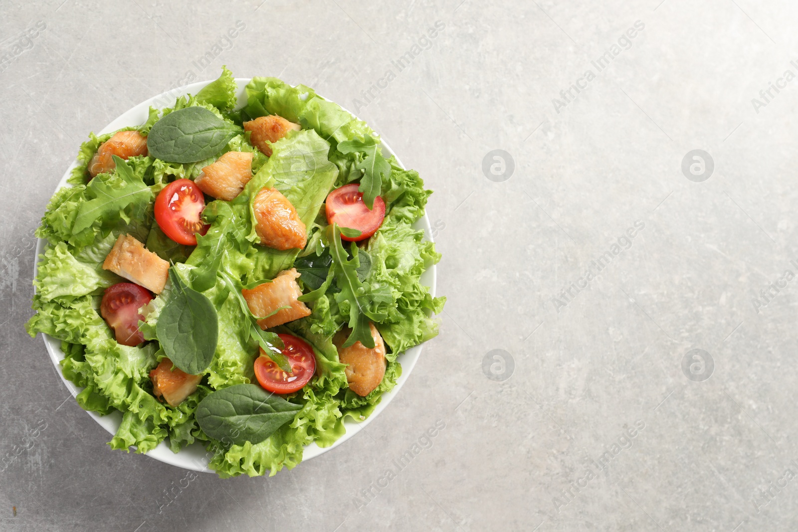 Photo of Delicious salad with chicken, cherry tomato and spinach on light grey table, top view. Space for text