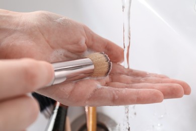 Photo of Woman washing makeup brush under stream of water in sink, closeup