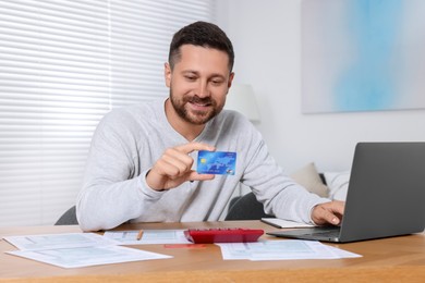 Man with credit card using laptop for paying taxes online at home