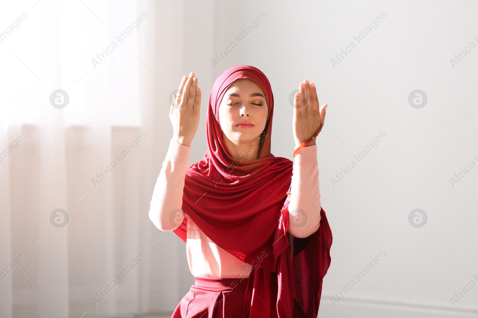 Photo of Young Muslim woman in hijab praying indoors