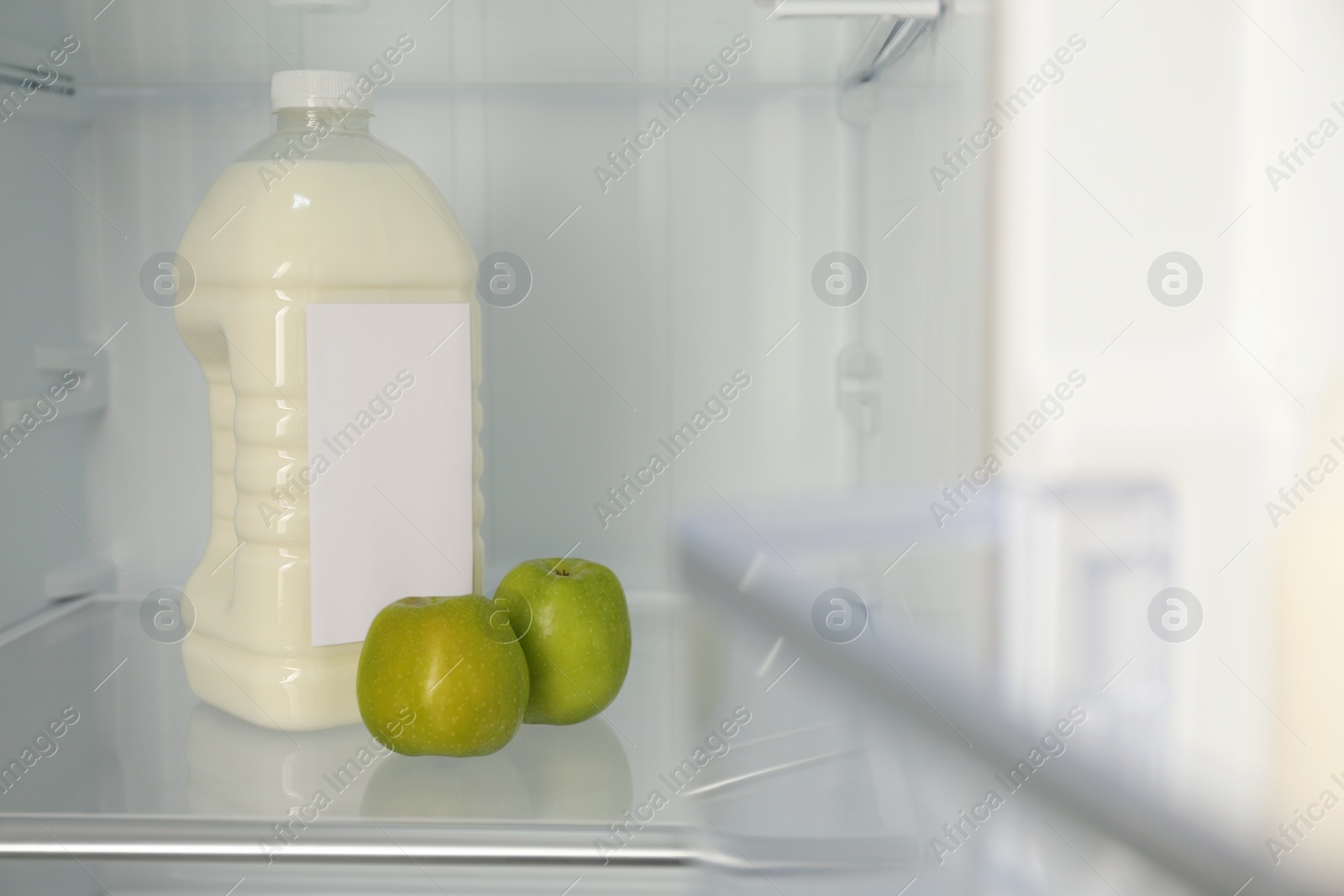 Photo of Gallon of milk and apples n refrigerator, closeup