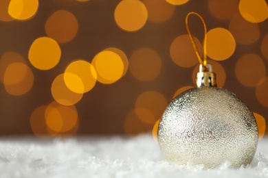Photo of Beautiful Christmas ball on snow against blurred festive lights. Space for text