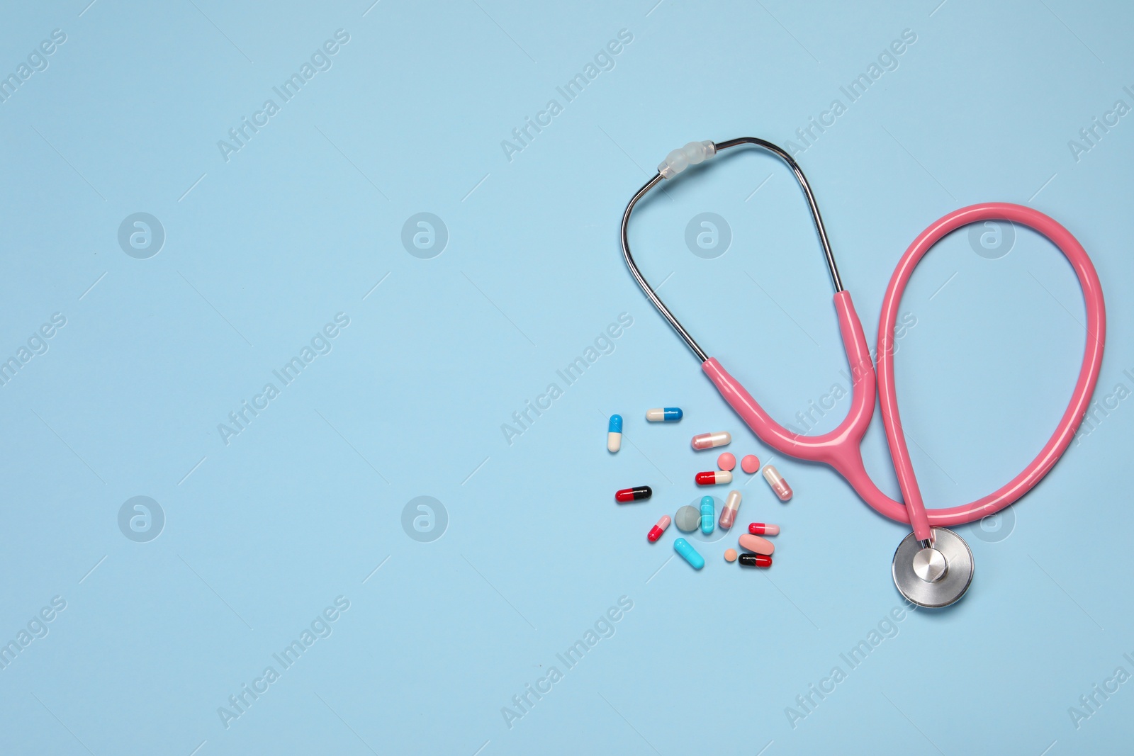 Photo of Stethoscope and pills on light blue background, top view. Space for text