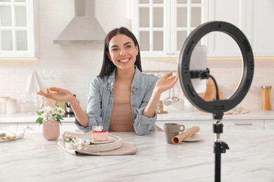 Photo of Blogger with tasty cake recording video in kitchen at home. Using ring lamp and smartphone