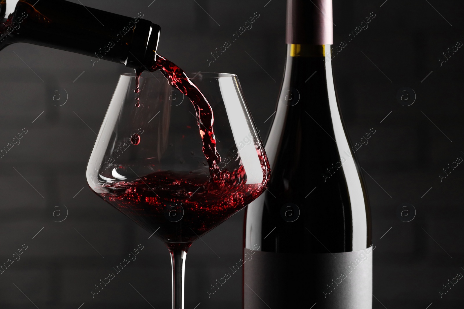 Photo of Pouring red wine into glass and bottles against brick wall background, closeup