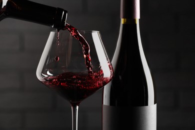 Photo of Pouring red wine into glass and bottles against brick wall background, closeup