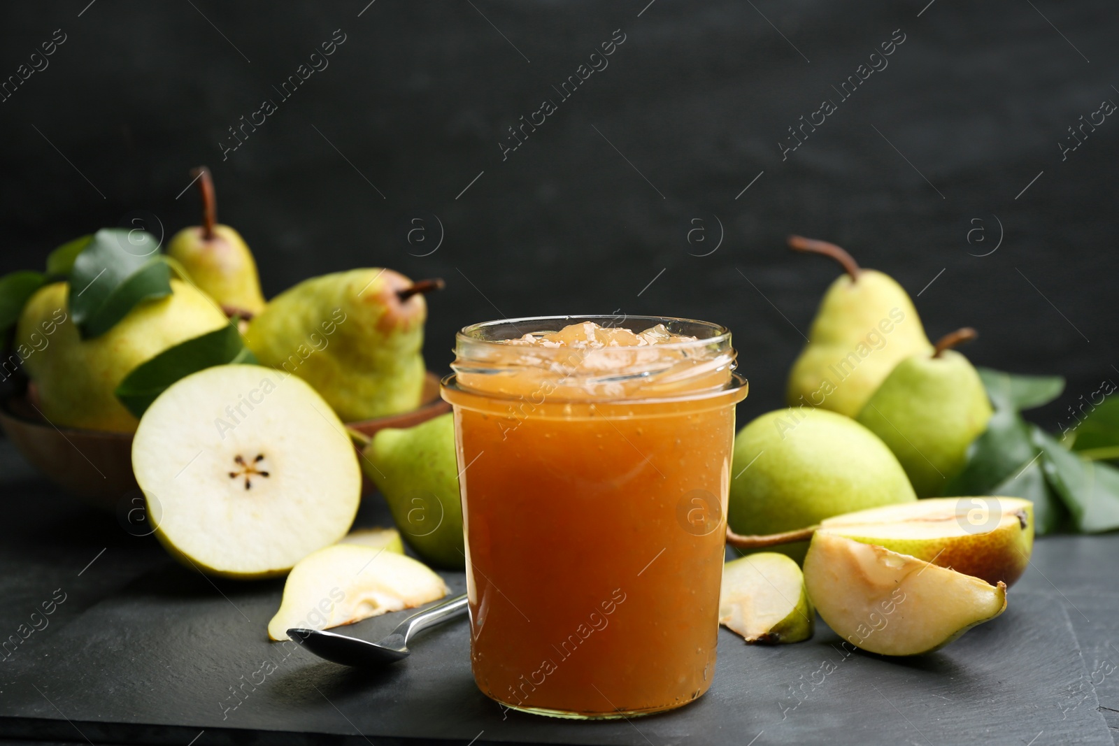 Photo of Tasty homemade pear jam and fresh fruits on black table