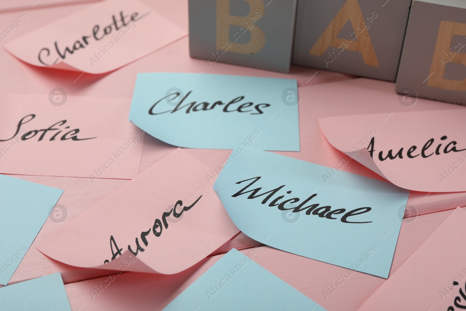 Photo of Paper stickers with different names on pink wooden table, closeup. Choosing baby's name