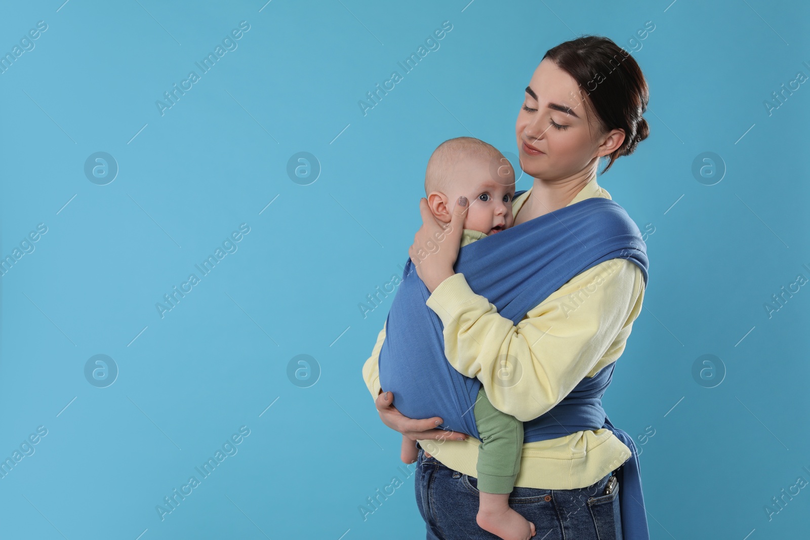 Photo of Mother holding her child in sling (baby carrier) on light blue background. Space for text