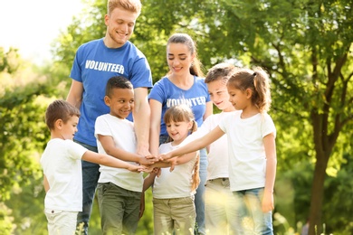 Group of kids joining hands with volunteers in park