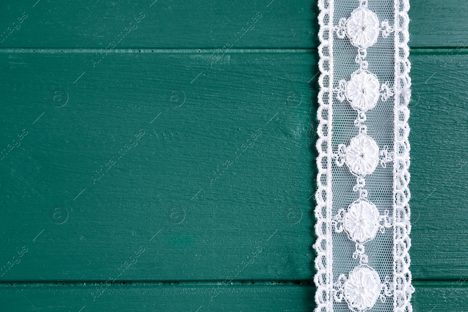 Photo of White lace on green wooden table, top view. Space for text