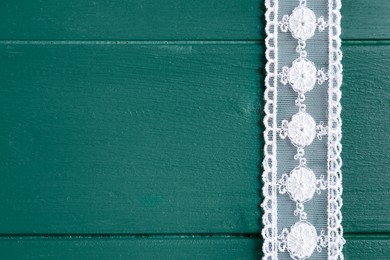 White lace on green wooden table, top view. Space for text