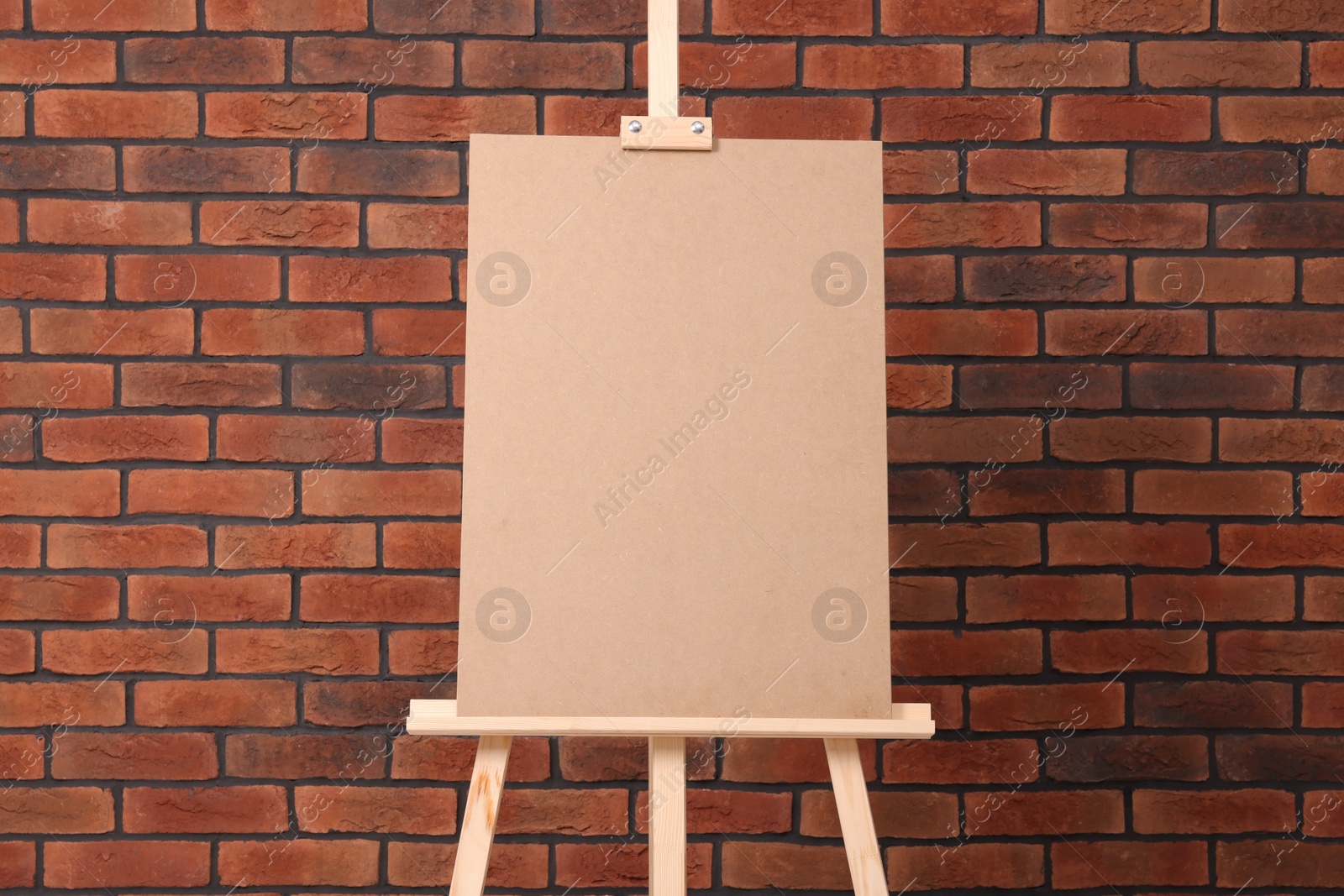 Photo of Wooden easel with blank board near brick wall