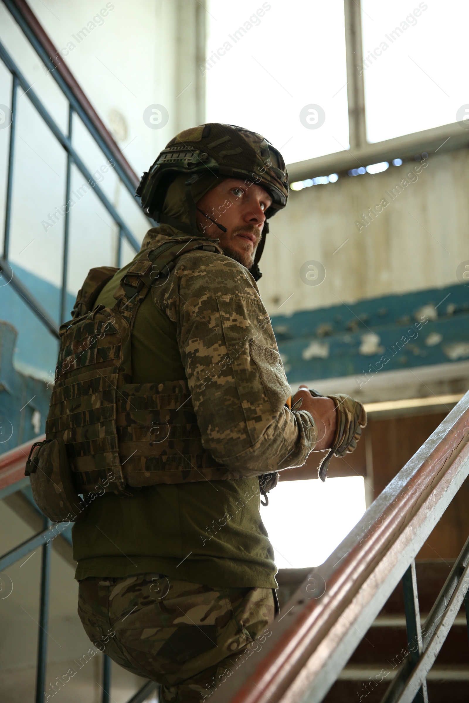 Photo of Military mission. Soldier in uniform on stairs inside abandoned building, low angle view