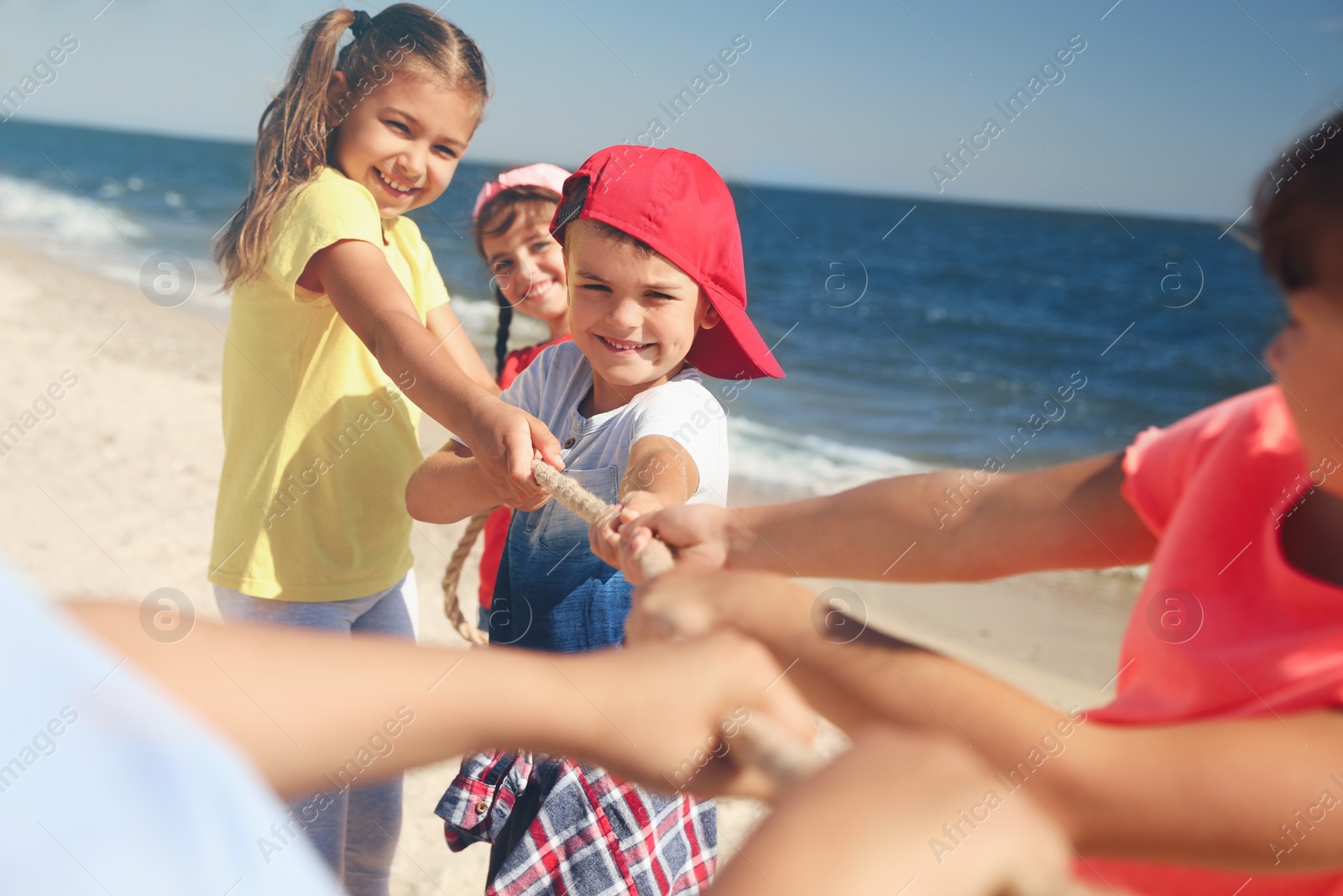 Photo of Cute children pulling rope during tug of war game on beach. Summer camp