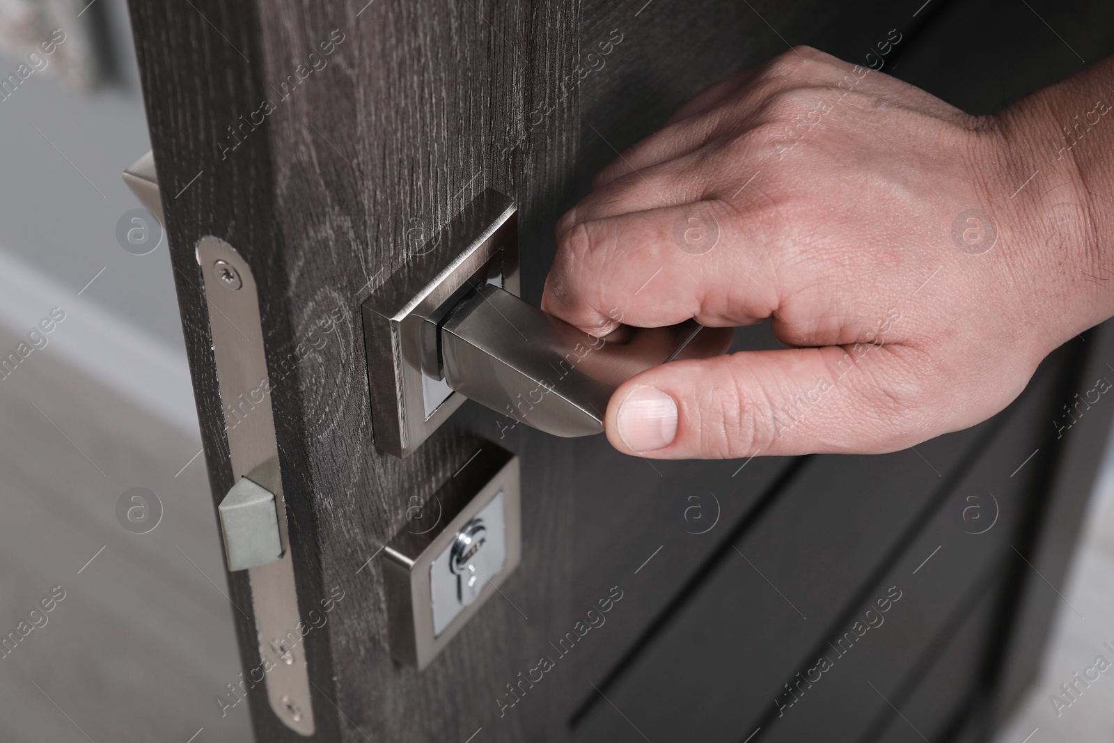 Photo of Man opening wooden door indoors, closeup of hand on handle