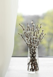 Photo of Beautiful pussy willow branches in glass vase on window sill indoors