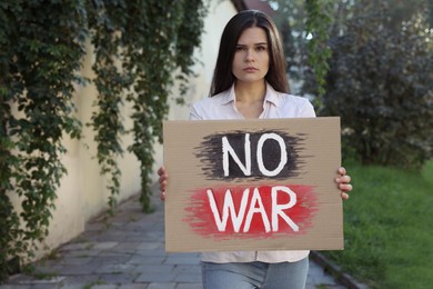Photo of Sad woman holding poster with words No War outdoors. Space for text