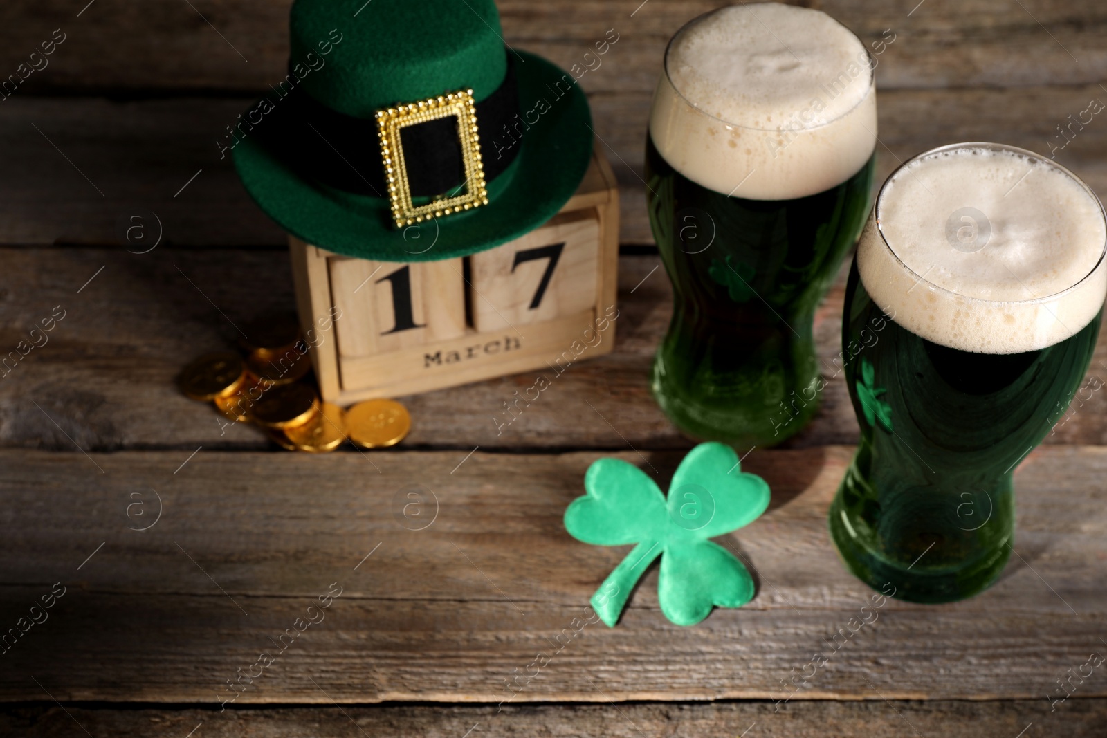 Photo of St. Patrick's day celebrating on March 17. Green beer, block calendar, leprechaun hat, gold coins and decorative clover leaf on wooden table