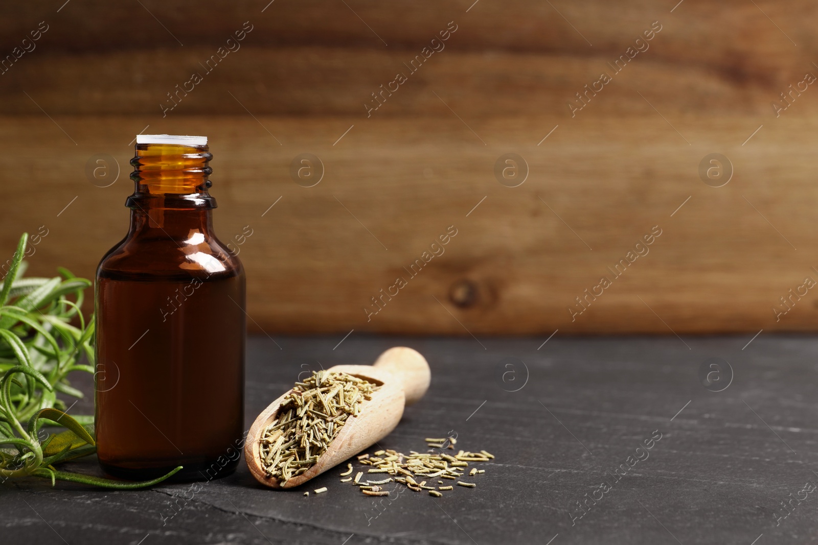 Photo of Bottle of essential oil, fresh and dry rosemary on gray table, space for text