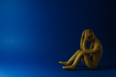 Photo of Plasticine figure of crying human on dark blue background. Space for text