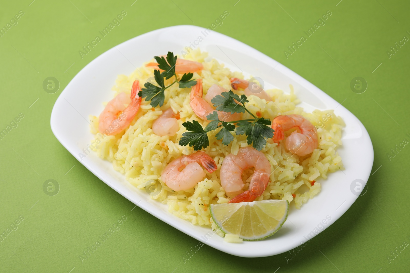 Photo of Delicious risotto with shrimps, lime and parsley on light green background