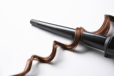 Photo of Modern clipless curling iron and brown hair lock on white background