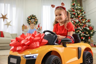 Cute little girl driving toy car in room decorated for Christmas