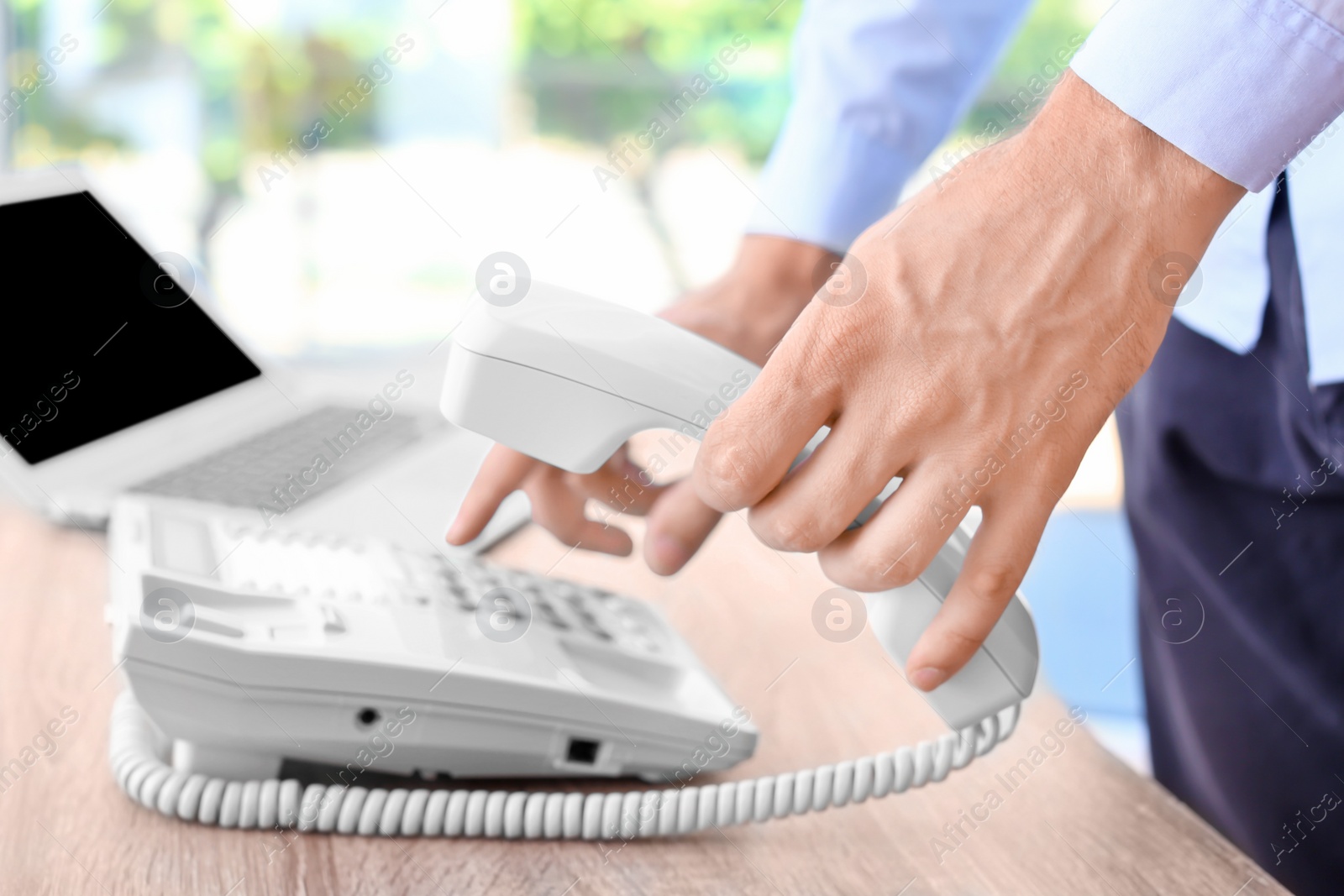 Photo of Man dialing number on telephone at workplace