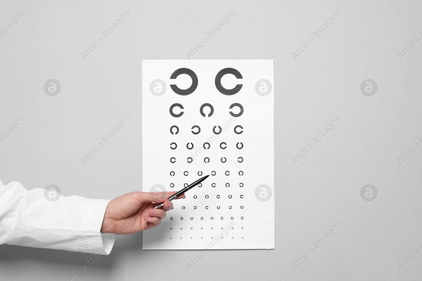 Photo of Ophthalmologist pointing at vision test chart on gray background, closeup