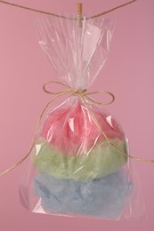 Photo of Packaged sweet cotton candy hanging on clothesline against pink background
