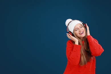 Photo of Young woman listening to music with headphones on dark blue background, space for text