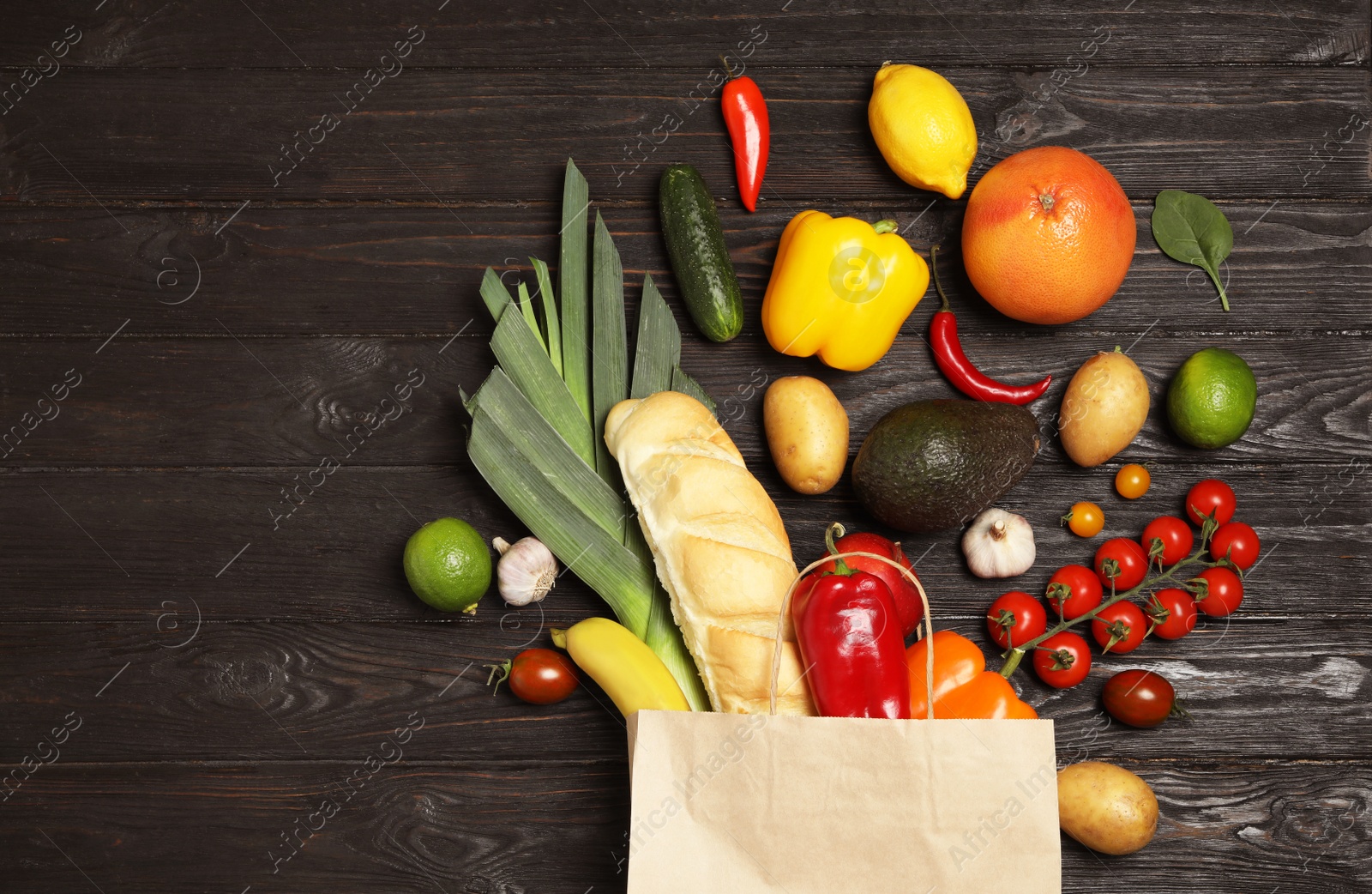 Photo of Shopping paper bag with different groceries on dark wooden background, flat lay