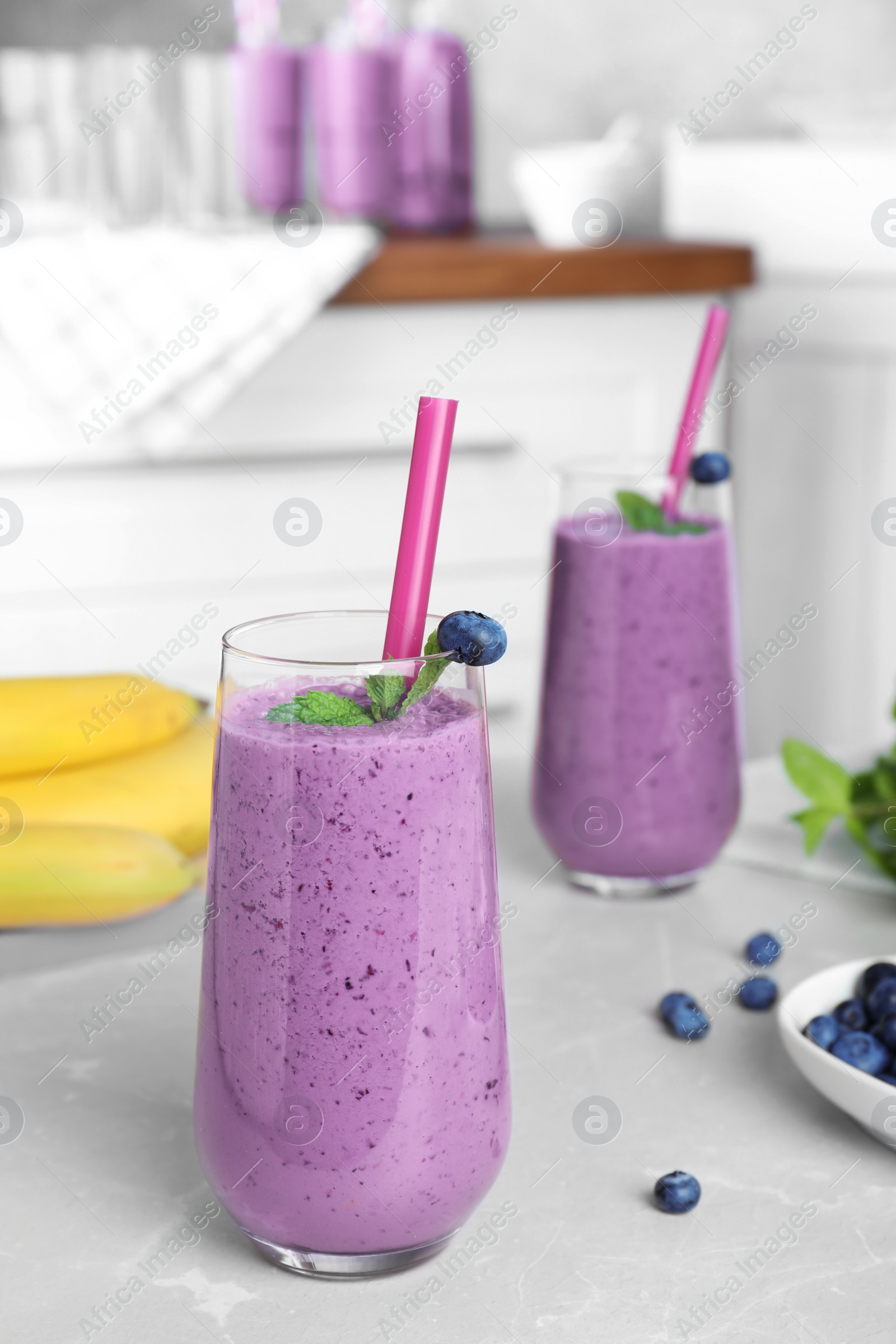 Photo of Glasses of delicious blueberry smoothie on light marble table in kitchen