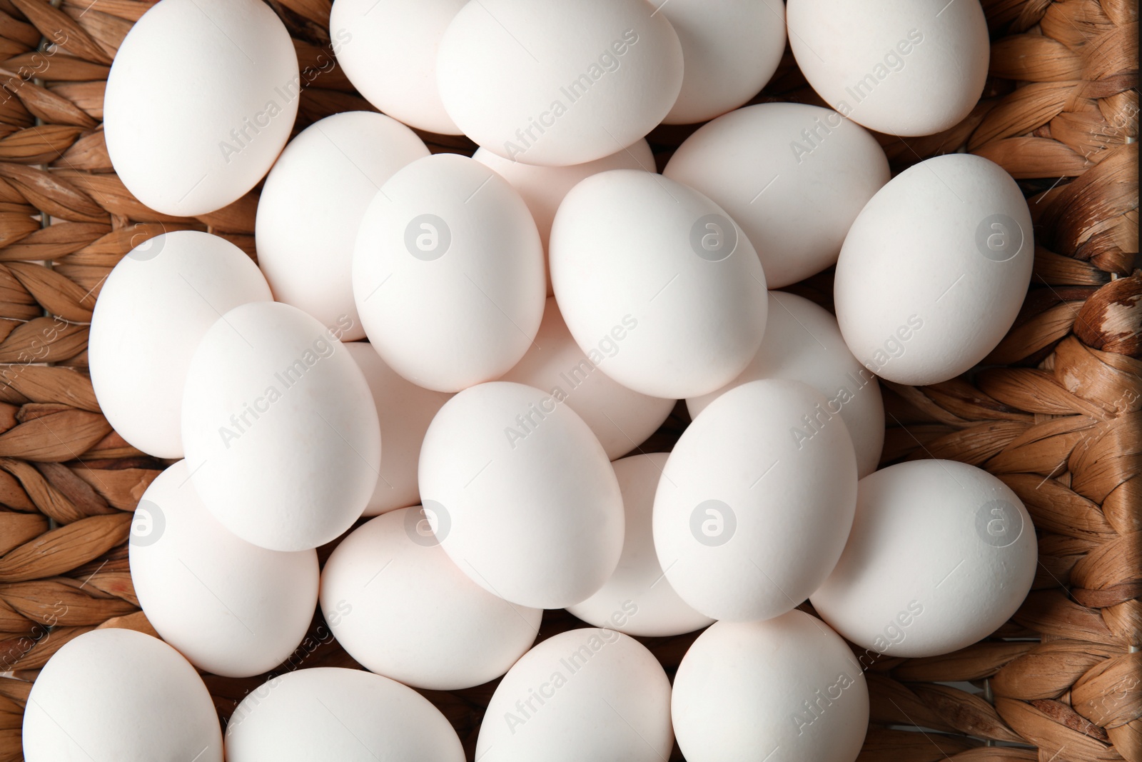 Photo of Pile of raw white chicken eggs in basket, top view