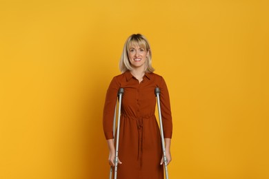 Photo of Portrait of happy woman with crutches on yellow background