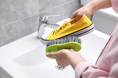 Woman washing stylish sneakers with brush in sink, closeup