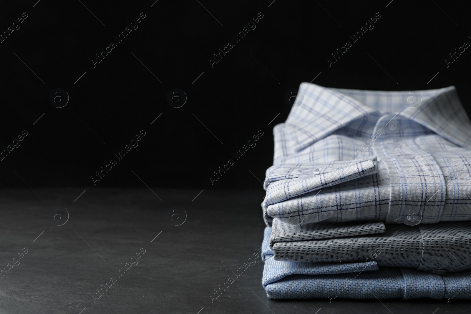 Photo of Stack of classic shirts on dark grey stone table. Space for text