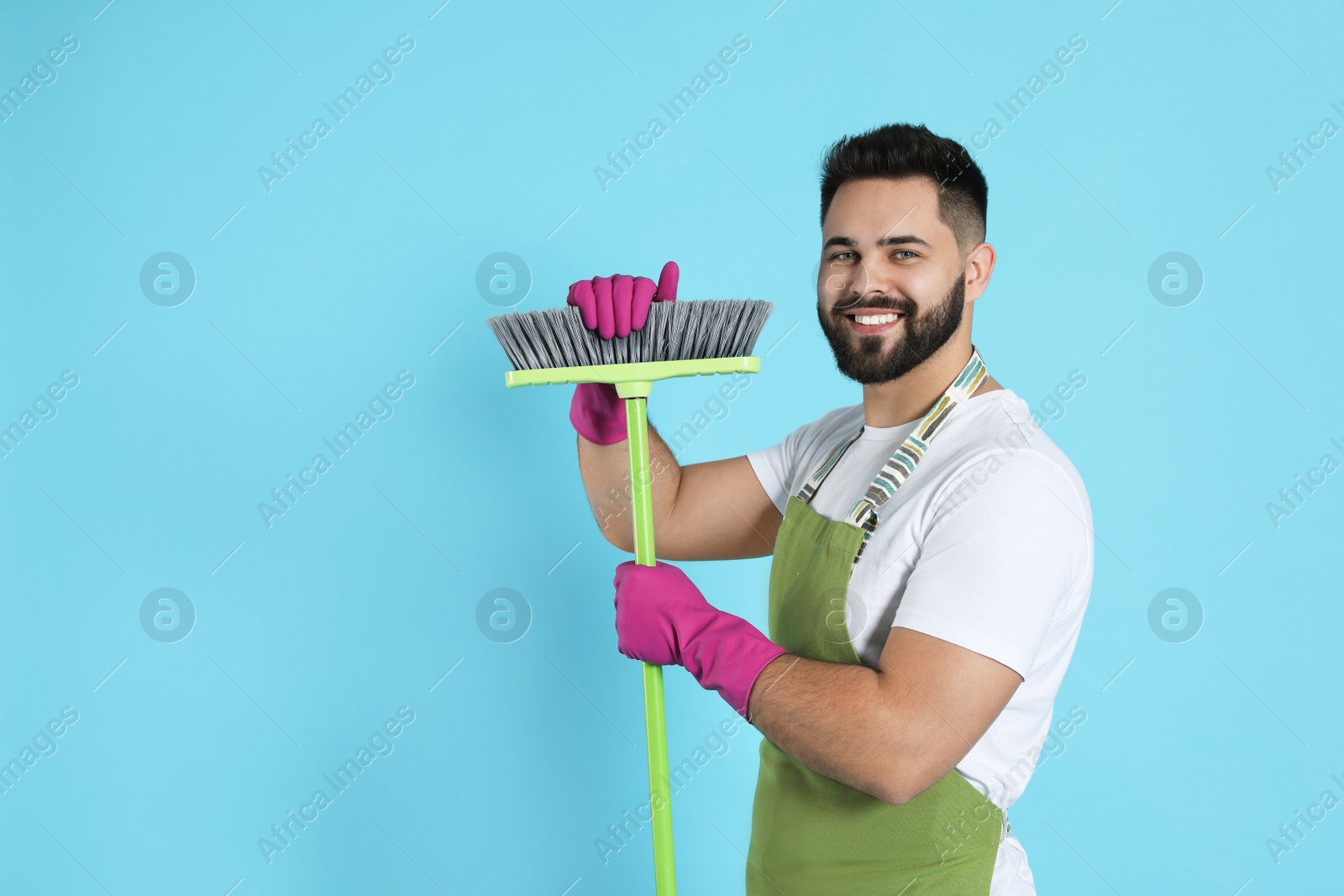 Photo of Young man with green broom on light blue background, space for text
