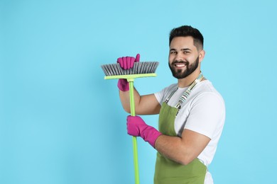 Young man with green broom on light blue background, space for text