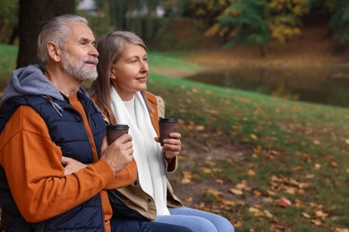Photo of Affectionate senior couple with cups of coffee in autumn park, space for text