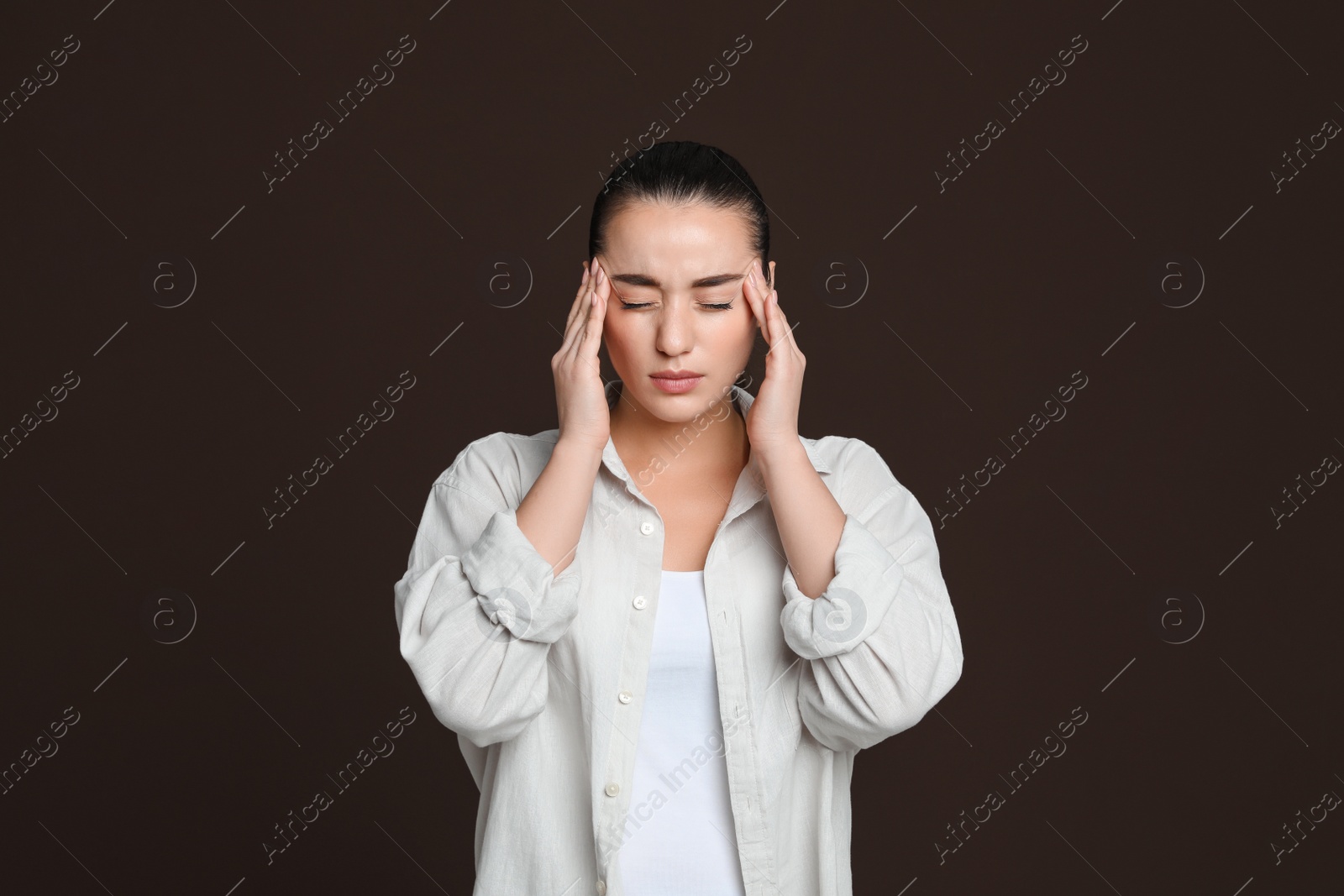 Photo of Young woman suffering from headache on dark brown background